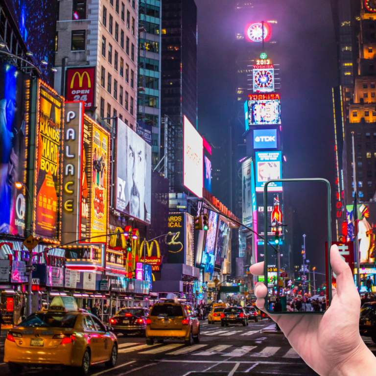Times Square at night with a hand holding a phone, representing social media visibility, digital campaigns, and content creation.
